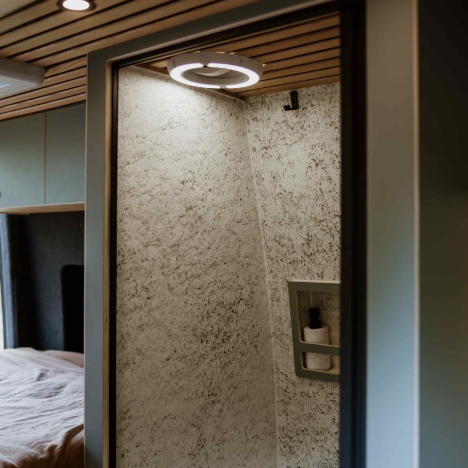 Cabine de douche intégrée dans le Mercedes Sprinter Aoraki – parois claires en feuille de pierre et robinetterie moderne.