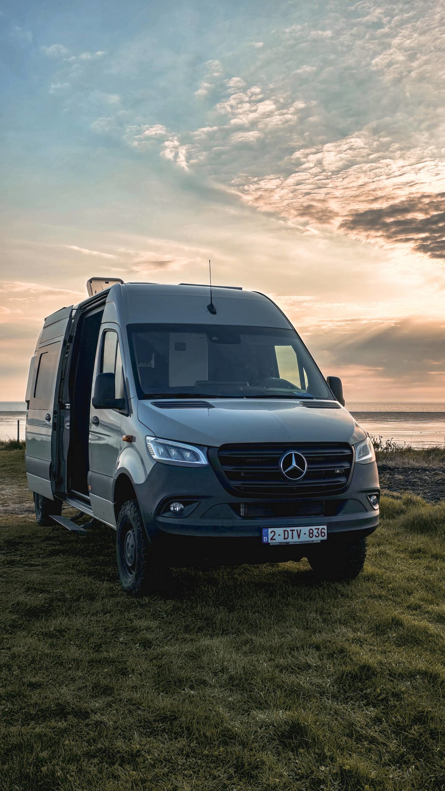 Mercedes Sprinter 4x4 aménagé pour la vanlife, stationné face à la mer du Nord au coucher du soleil.