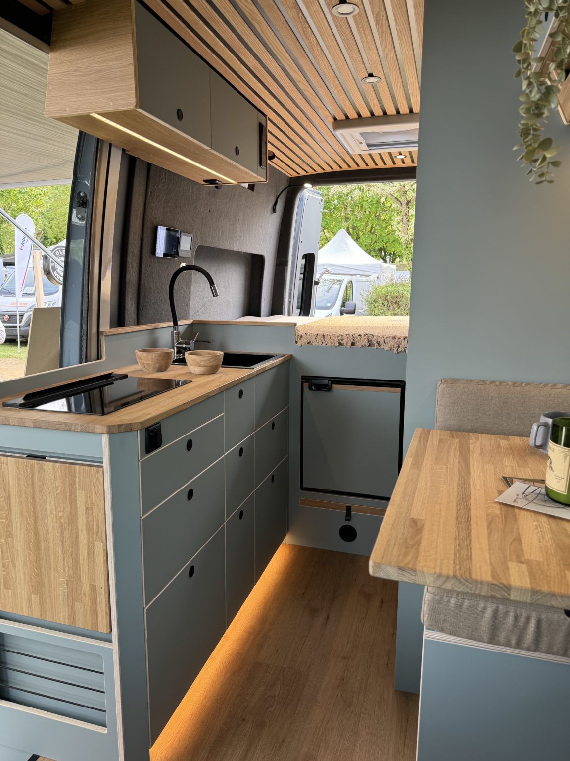 Intérieur d’un Mercedes Sprinter L2H2 aménagé sur mesure – configuration Aoraki pour 2 personnes, avec cuisine équipée, mobilier en bois clair et éclairage d’ambiance chaleureux – création OLEY WORKSHOP.