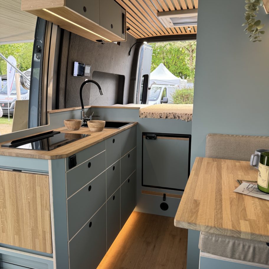 Intérieur d’un Mercedes Sprinter L2H2 aménagé sur mesure – configuration Aoraki pour 2 personnes, avec cuisine équipée, mobilier en bois clair et éclairage d’ambiance chaleureux – création OLEY WORKSHOP.