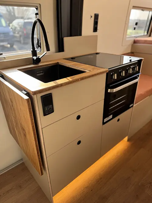 Cuisine compacte de fourgon aménagé avec évier en bois et plaque de cuisson avec four intégré.