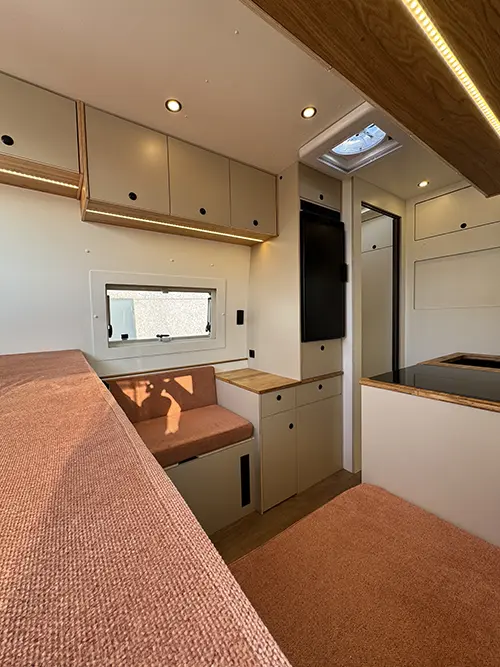 Intérieur aménagé d’un fourgon avec banquettes en tissu terracotta, rangements intégrés et cuisine compacte.