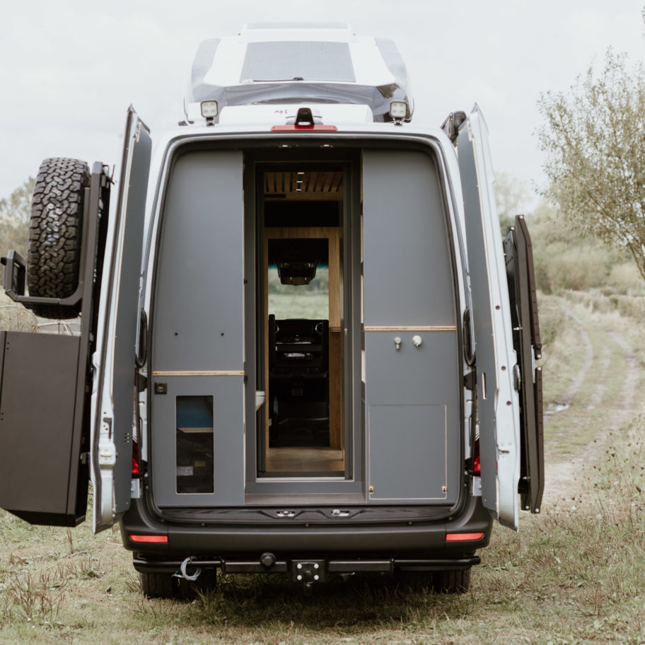 Vue arrière du Mercedes Sprinter 4x4 L4H2 519 CDI “Signature” aménagé par OLEY WORKSHOP – accès soute, rangements techniques intégrés et finitions en bois clair et gris mat.