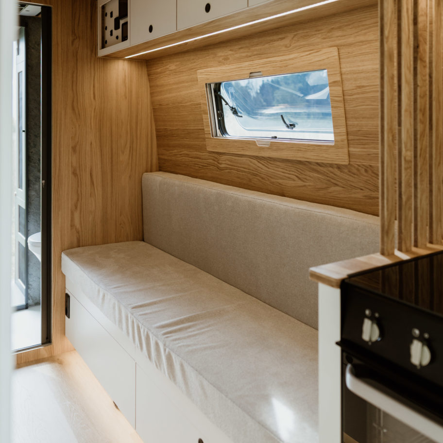 Coin salon d’un fourgon aménagé avec banquette longue et placards en bois.