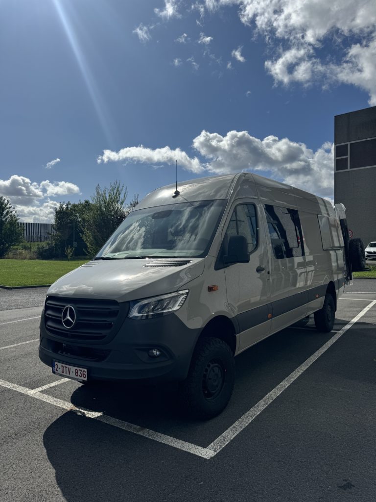 Fourgon Mercedes Sprinter garé sur un parking sous un ciel ensoleillé.