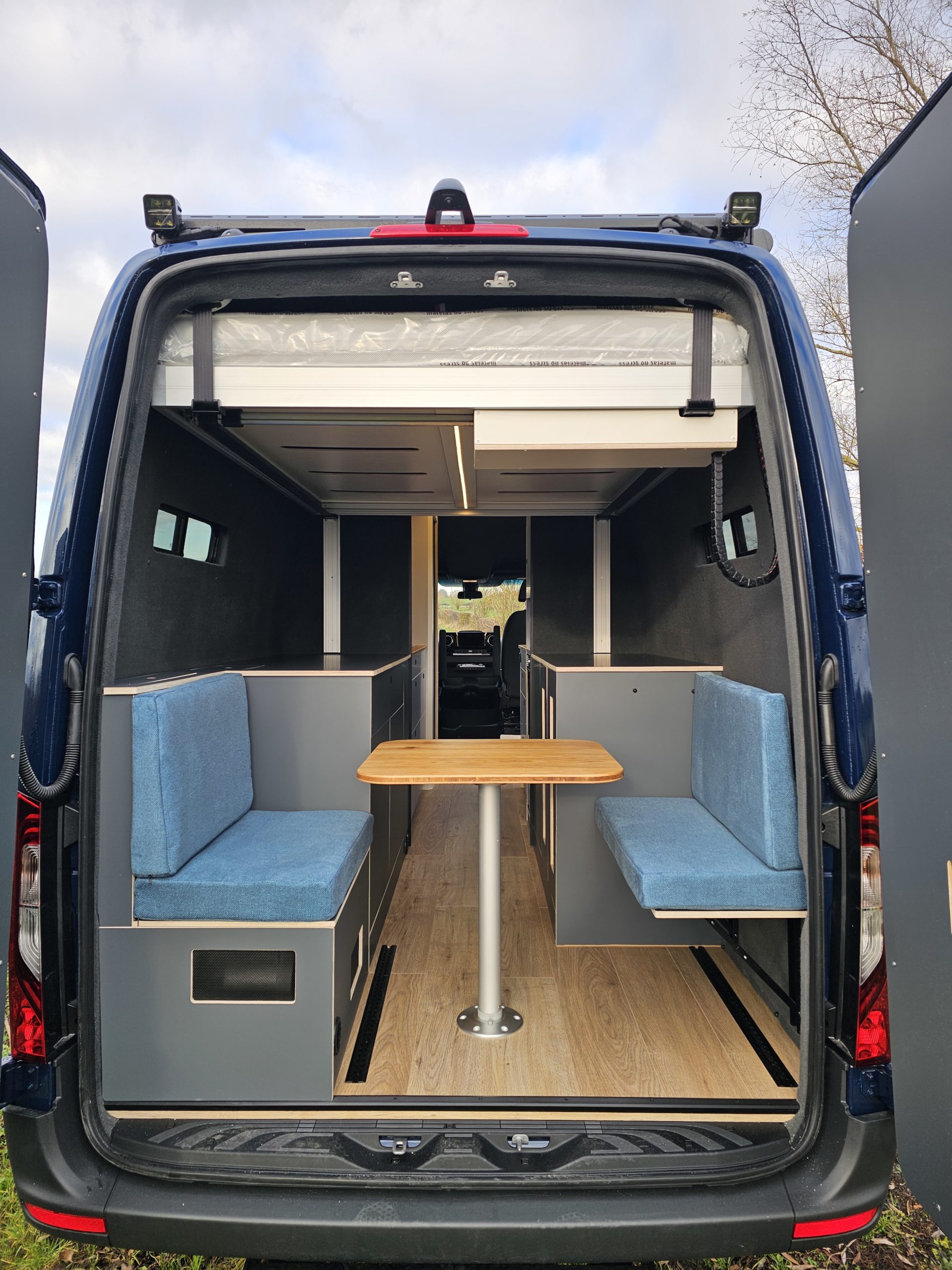 Intérieur du fourgon aménagé avec banquettes, table centrale et lit relevable.