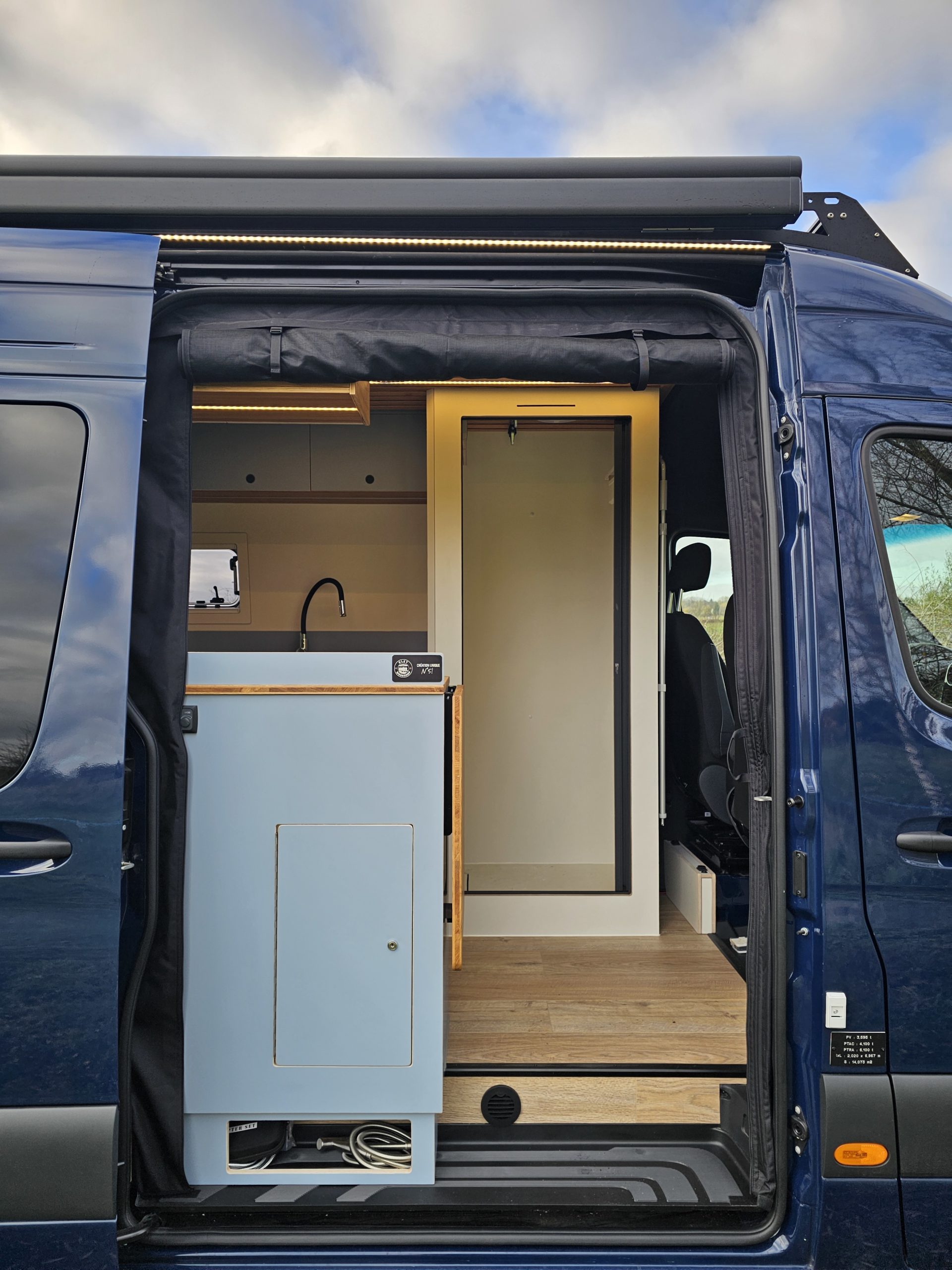 Entrée latérale du fourgon aménagé avec meuble bleu, éclairage LED et accès à la cabine.