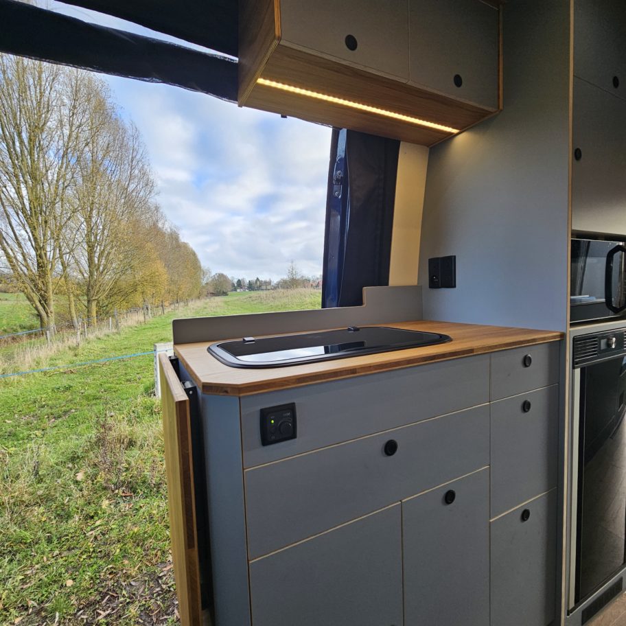 Plan de travail en bois avec évier et vue sur l’extérieur du fourgon.