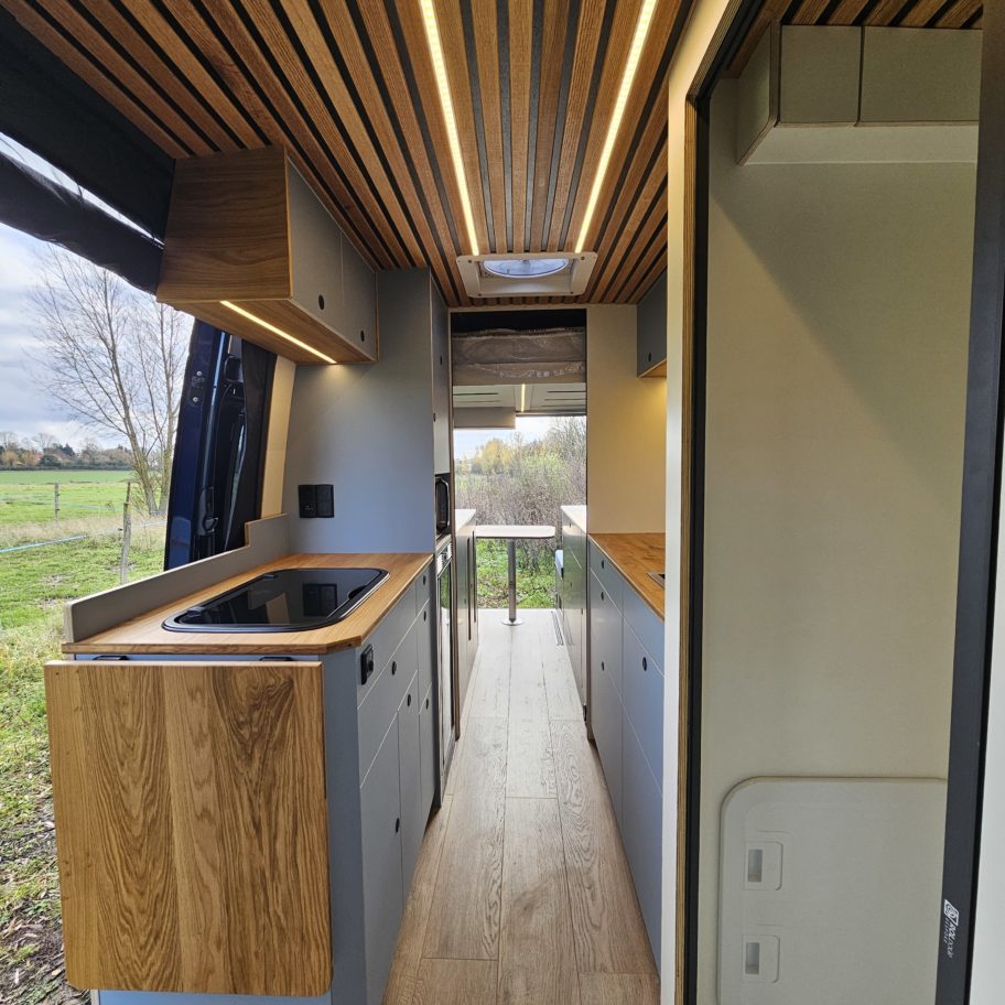 Couloir du fourgon avec plafond en lattes bois et meuble de cuisine.