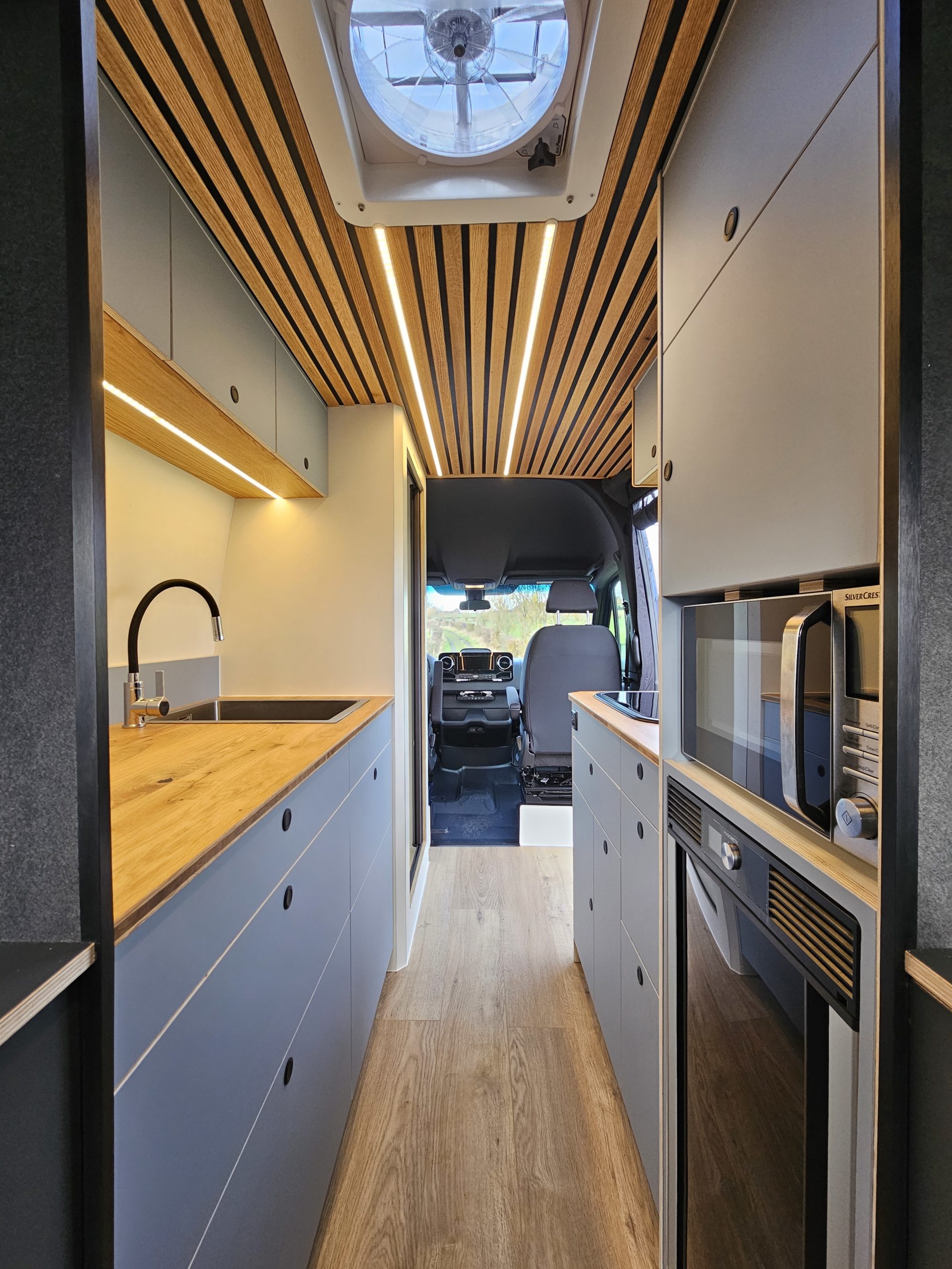 Intérieur du fourgon aménagé avec cuisine, rangements et plafond en lattes bois.
