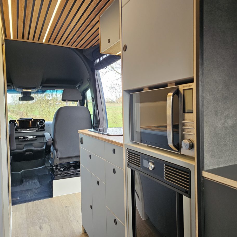 Cuisine du fourgon avec frigo intégré et vue sur la cabine.