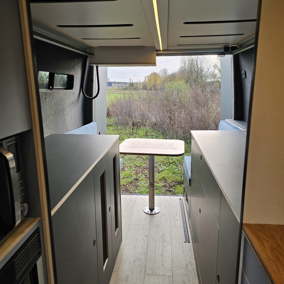 Perspective intérieure du fourgon avec table centrale et rangements.