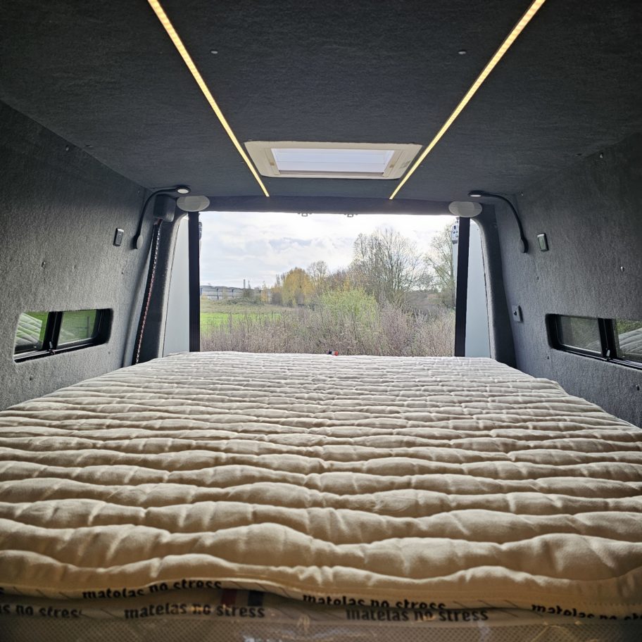 Espace nuit du fourgon aménagé avec matelas et vue extérieure.