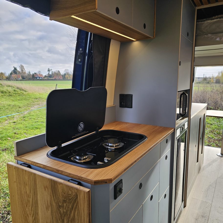 Bloc cuisson du fourgon avec plaque, fenêtre latérale et meuble bois.