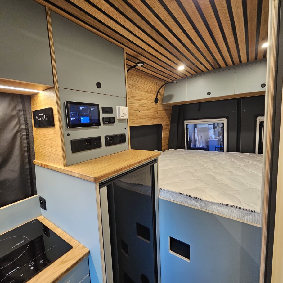 Intérieur d’un van Mercedes Sprinter aménagé avec coin cuisine, rangements et lit double à l'arrière