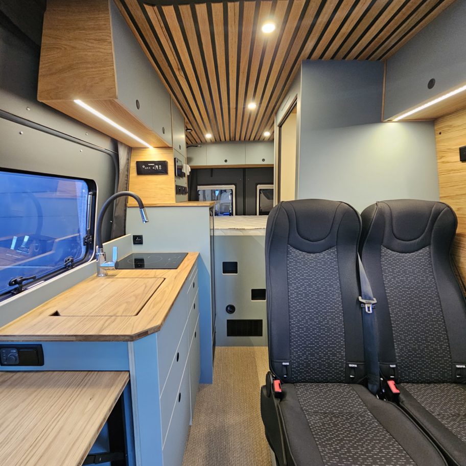 Intérieur d’un van Mercedes Sprinter aménagé avec cuisine latérale, plan de travail en bois et deux sièges avant.