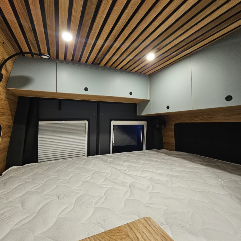 Espace nuit d’un van Mercedes Sprinter aménagé avec lit double, rangements et plafond en bois.