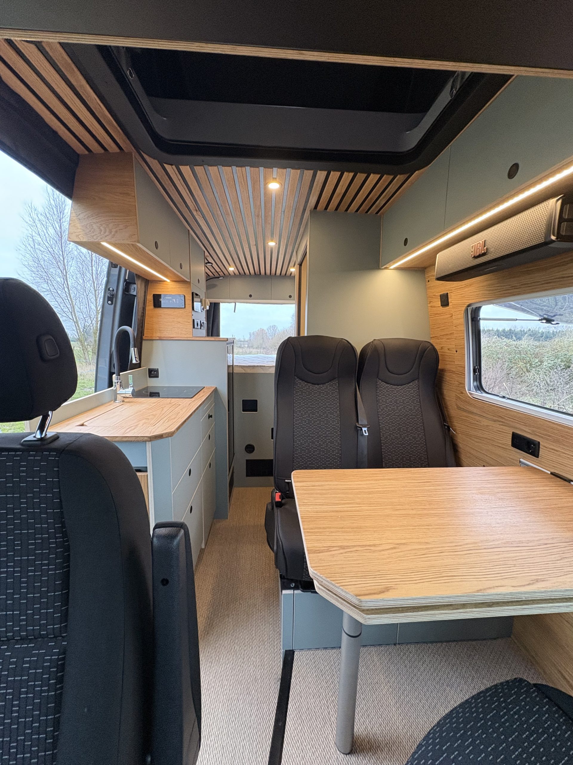 Intérieur de van aménagé moderne avec table en bois, sièges face à face et rangements intégrés.