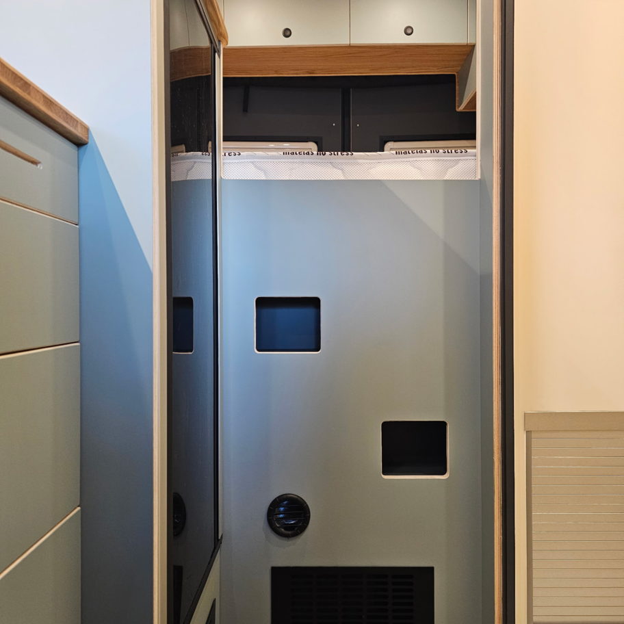Meuble technique en bois contreplaqué dans un van Mercedes Sprinter aménagé avec grilles d’aération et trappes d’accès.