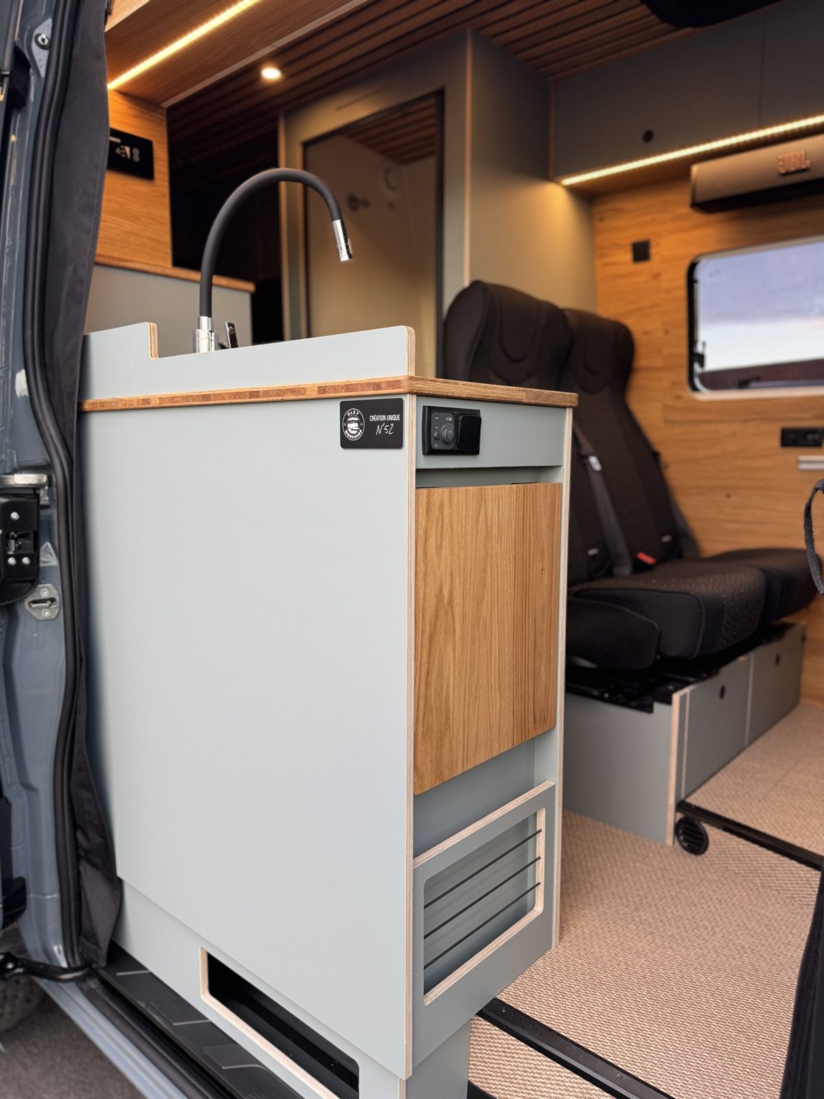 Intérieur d’un van Mercedes Sprinter aménagé avec kitchenette compacte, évier, rangements en bois et siège passager.