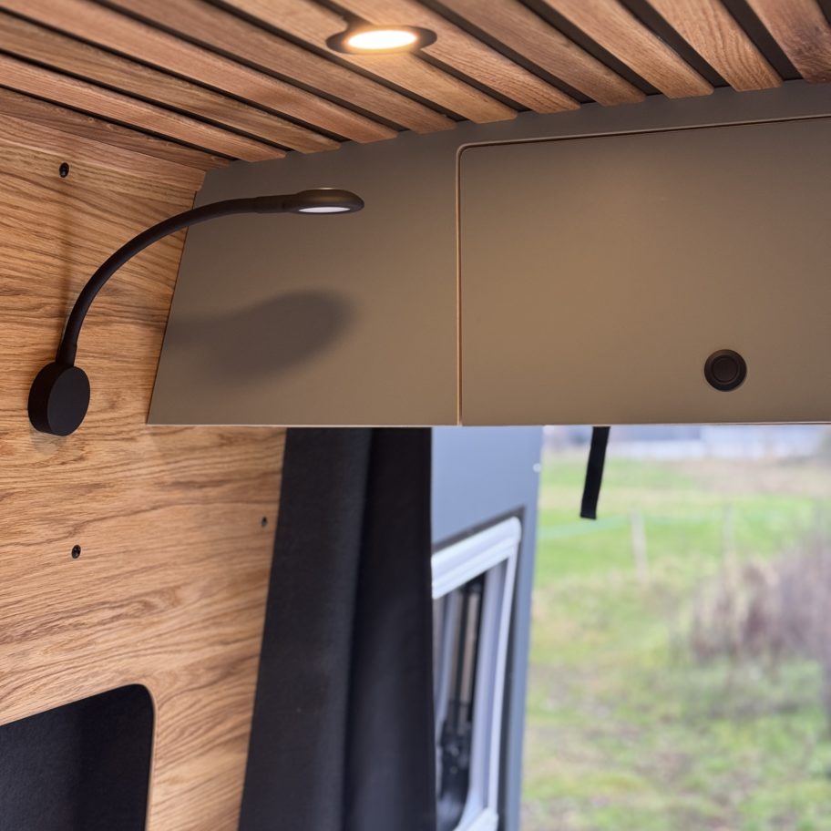 Lampe de lecture flexible installée au-dessus du lit dans un van Mercedes Sprinter aménagé.
