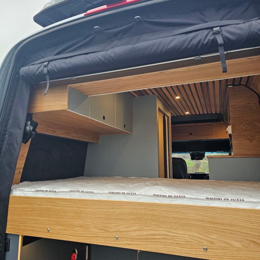 Vue arrière d’un van Mercedes Sprinter aménagé avec lit surélevé et ouverture du hayon.