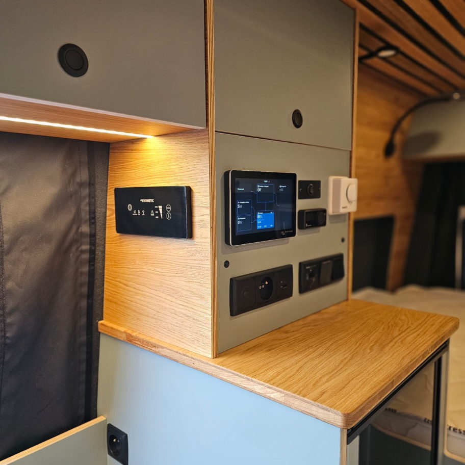 Panneau de contrôle électrique et rangements d’un van Mercedes Sprinter aménagé avec plan de travail en bois.