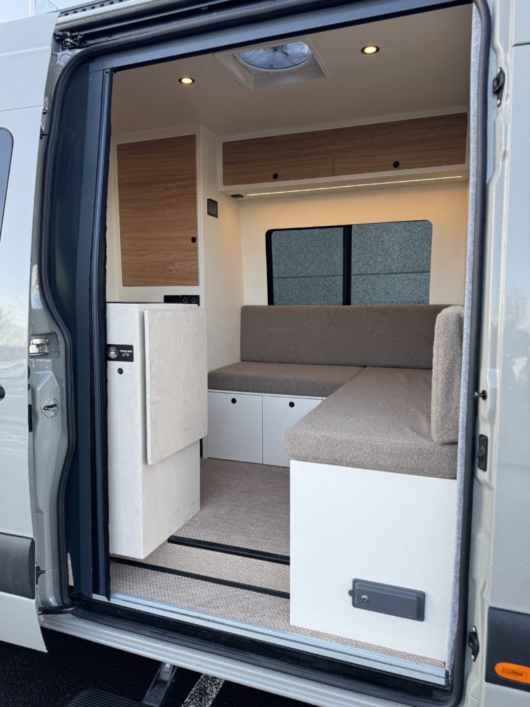 Intérieur d’un van aménagé avec banquettes, rangements en bois clair et espace de couchage modulable.