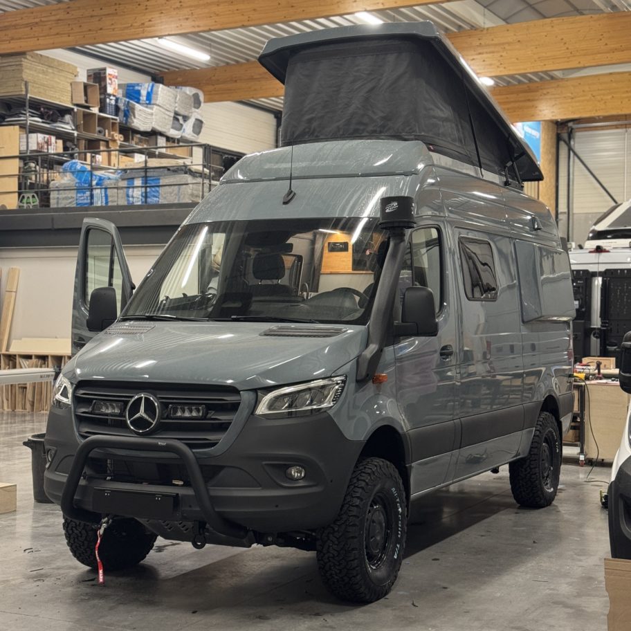 Fourgon Mercedes Sprinter 4x4 aménagé avec toit relevable ouvert, équipé pour le voyage tout-terrain, dans un atelier de fabrication.