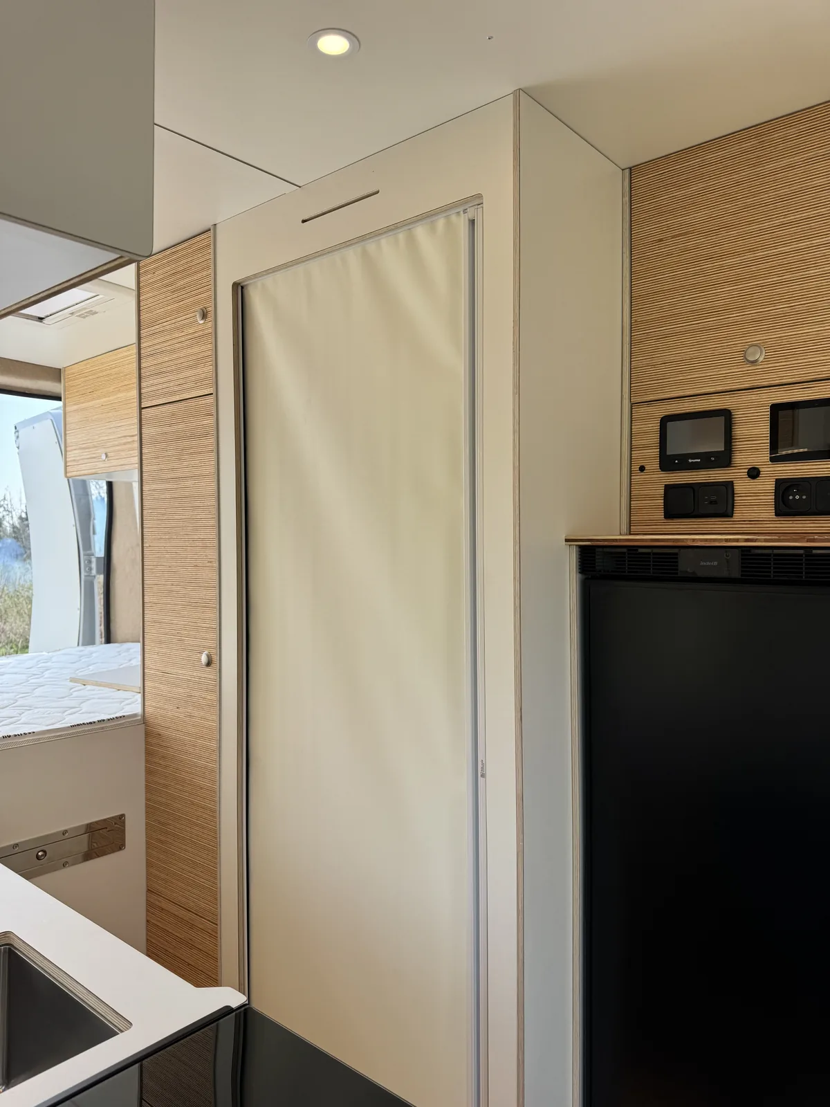 Salle d'eau du KAURI — cabine douche cylindrique blanche, habillage chêne, frigo Dometic 90 L, atelier Oley Workshop Roncq (59) Hauts-de-France