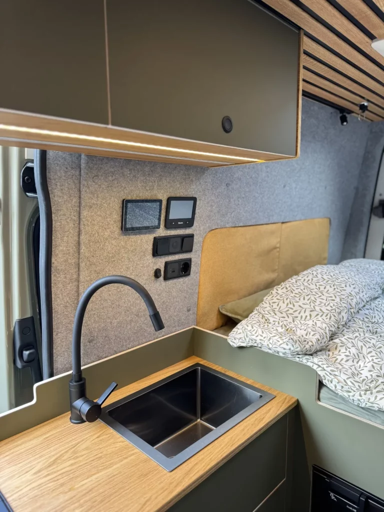 Cuisine du Sprinter 4x4 aménagé autonome Foxiii avec évier inox et couchage en arrière-plan — Oley Workshop