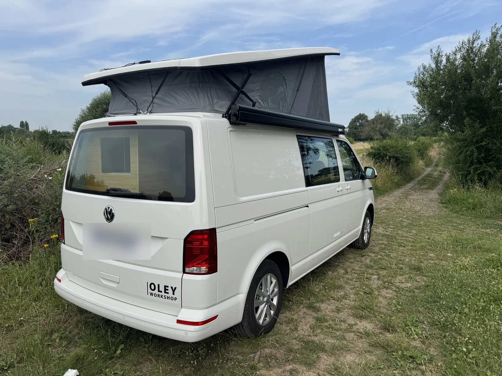 Toit relevable ouvert sur un VW T6 aménagé par Oley Workshop, en bivouac sur un chemin de campagne