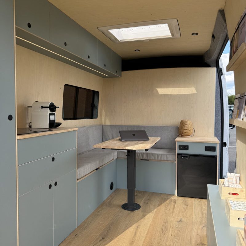 Aménagement sur mesure d’un fourgon en bureau mobile associatif avec banquette en U, table centrale et rangements intégrés.